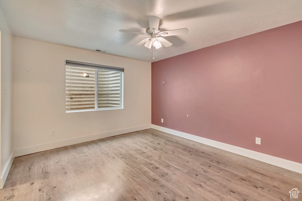 Empty room featuring baseboards, a ceiling fan, visible vents, and wood finished floors