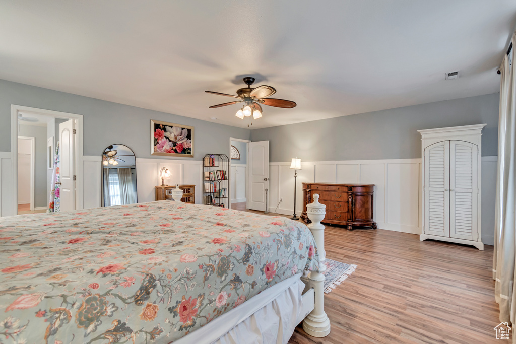 Bedroom with visible vents, a decorative wall, wainscoting, ceiling fan, and light wood-style floors
