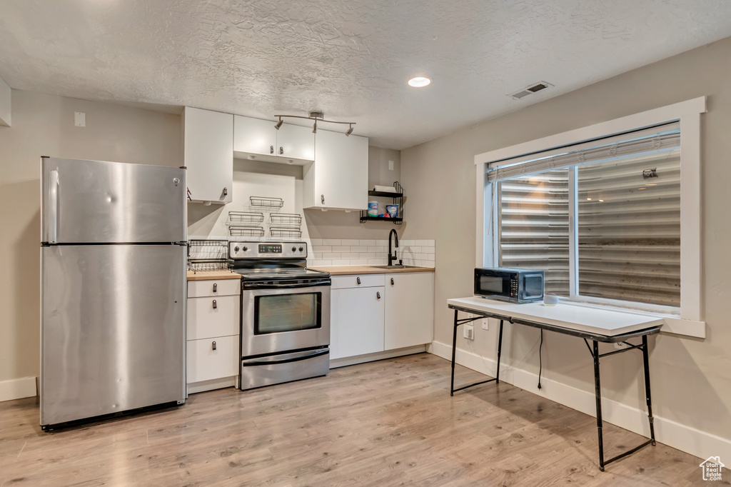 Kitchen with light wood finished floors, a sink, white cabinets, baseboards, and appliances with stainless steel finishes