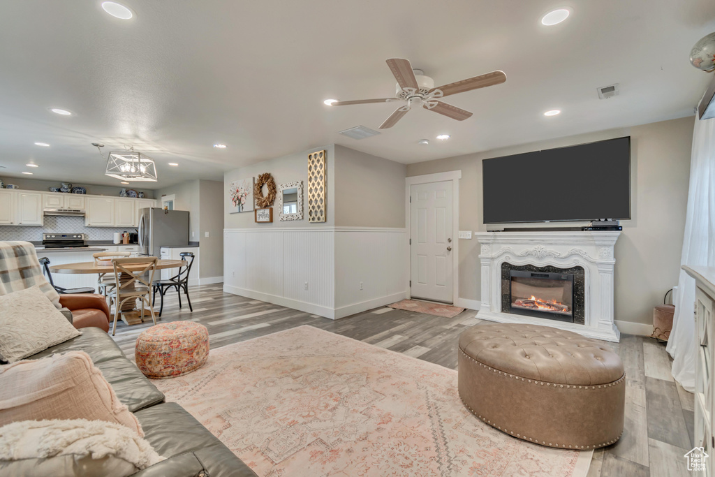 Living area with light wood-style flooring, a ceiling fan, visible vents, a glass covered fireplace, and recessed lighting