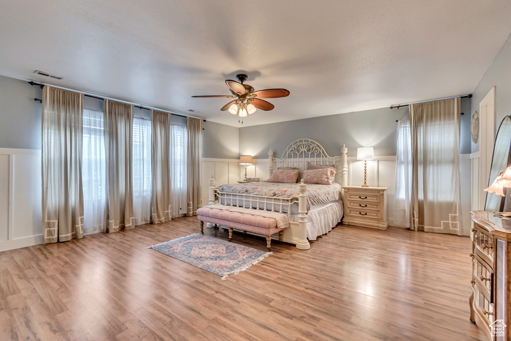 Bedroom featuring a decorative wall, a wainscoted wall, wood finished floors, visible vents, and ceiling fan