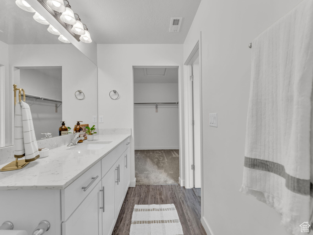 Full bathroom with wood finished floors, visible vents, baseboards, vanity, and a spacious closet
