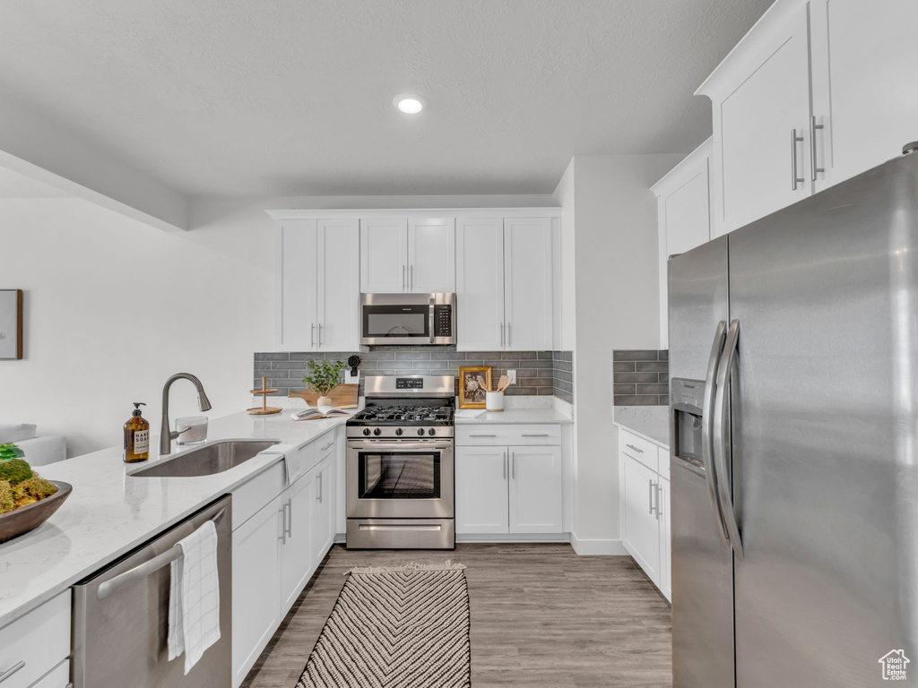 Kitchen featuring light stone counters, a sink, light wood-style floors, stainless steel appliances, and white cabinets