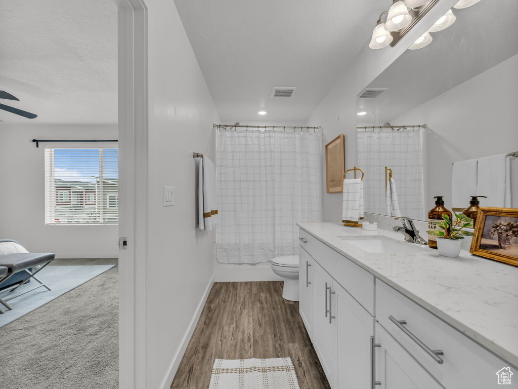 Full bathroom featuring toilet, wood finished floors, vanity, visible vents, and baseboards
