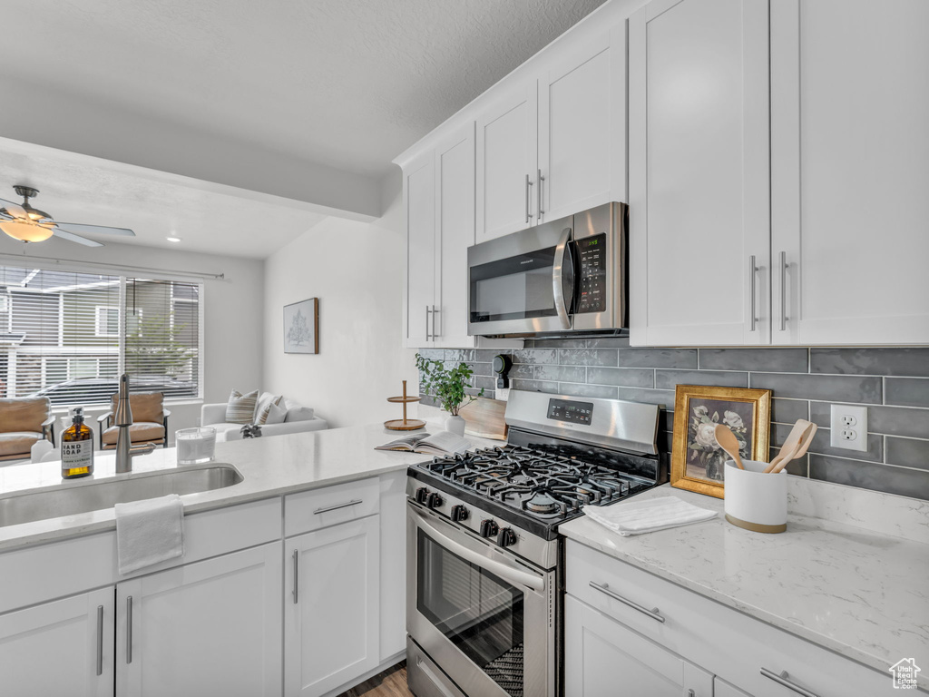 Kitchen with ceiling fan, a sink, white cabinetry, open floor plan, and appliances with stainless steel finishes