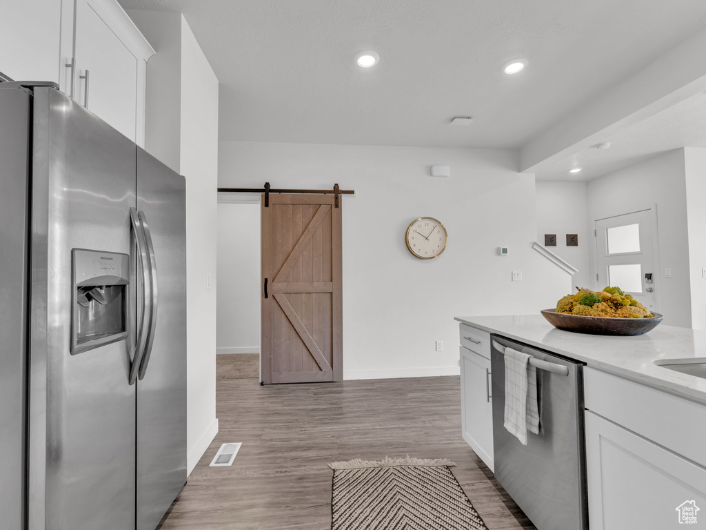 Kitchen featuring a barn door, baseboards, visible vents, white cabinetry, and stainless steel appliances