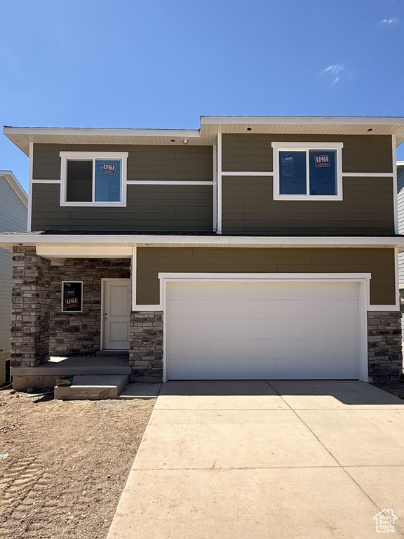 View of front facade featuring stone siding, an attached garage, and driveway