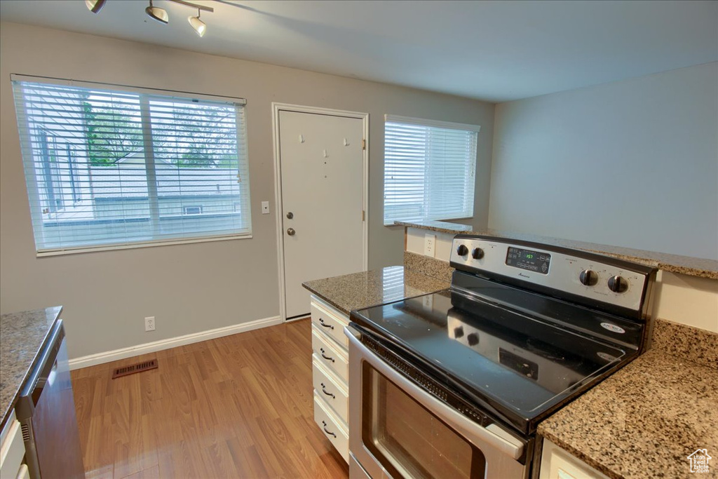 Kitchen with baseboards, light stone counters, white cabinets, light wood-type flooring, and electric range