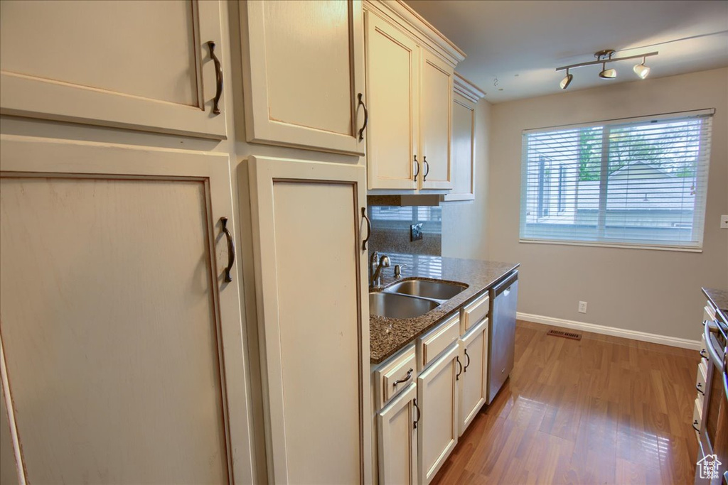Kitchen featuring light wood finished floors, a sink, dark stone counters, stainless steel dishwasher, and baseboards