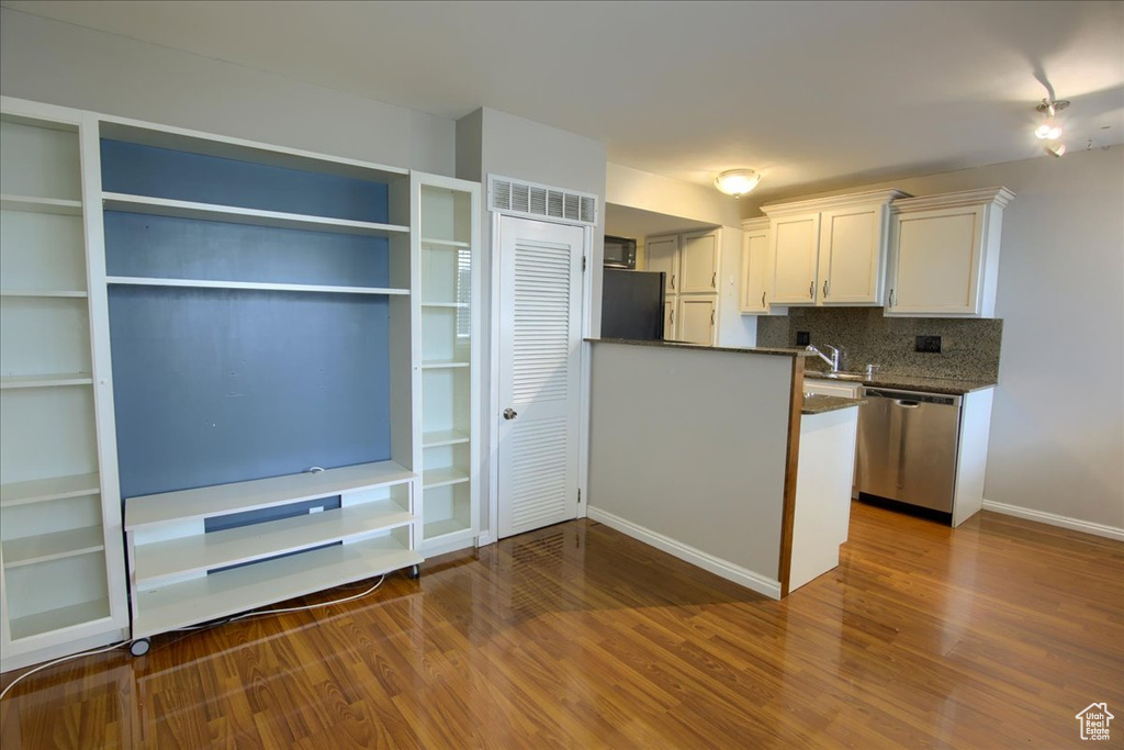 Kitchen featuring wood finished floors, decorative backsplash, white cabinets, stainless steel dishwasher, and baseboards