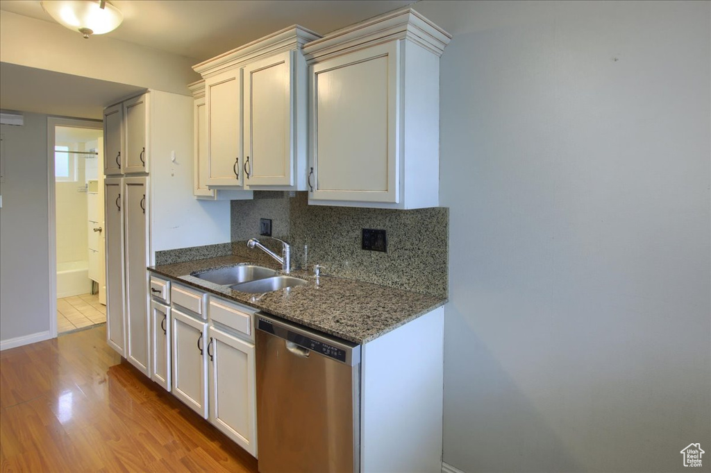 Kitchen with a sink, stone countertops, tasteful backsplash, wood finished floors, and stainless steel dishwasher