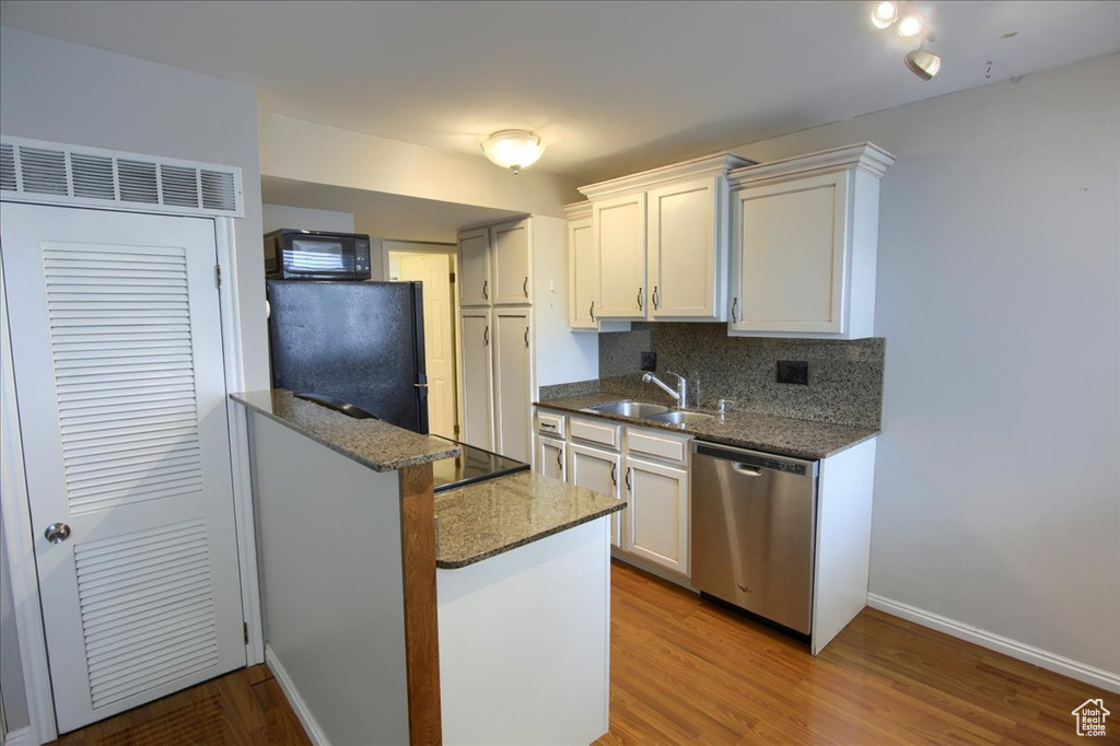 Kitchen featuring a sink, dark stone countertops, wood finished floors, black appliances, and decorative backsplash