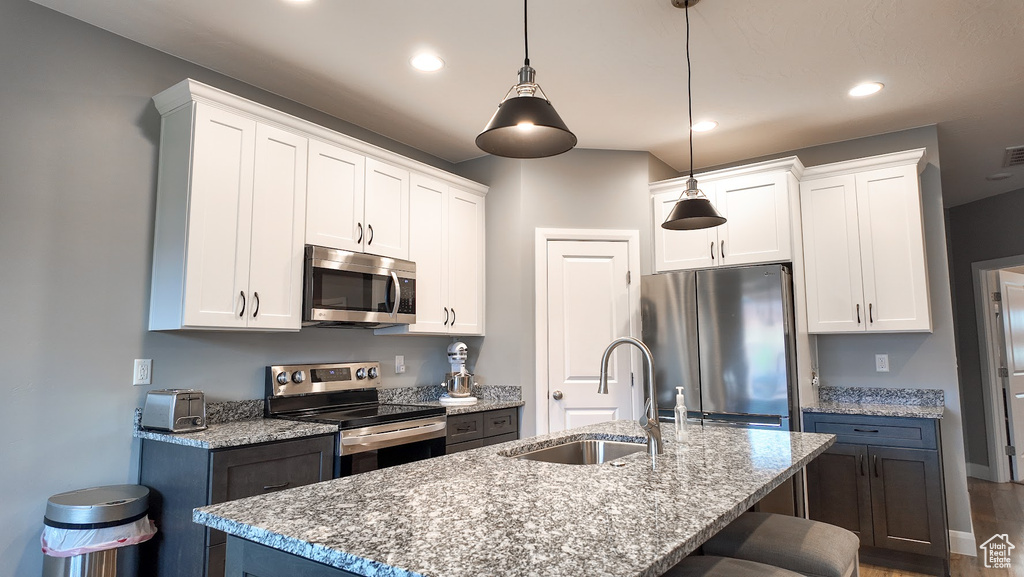 Kitchen featuring white cabinets, stainless steel appliances, a kitchen bar, and a sink