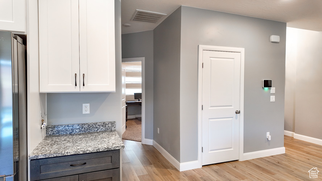 Interior space featuring freestanding refrigerator, light wood-style flooring, baseboards, visible vents, and white cabinets