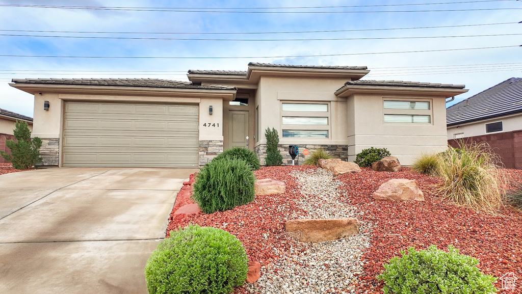 Prairie-style home with stone siding, concrete driveway, stucco siding, and a tiled roof