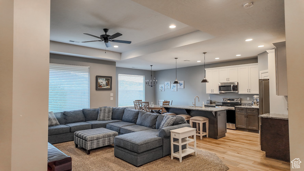 Living area with light wood-style floors, ceiling fan with notable chandelier, and recessed lighting