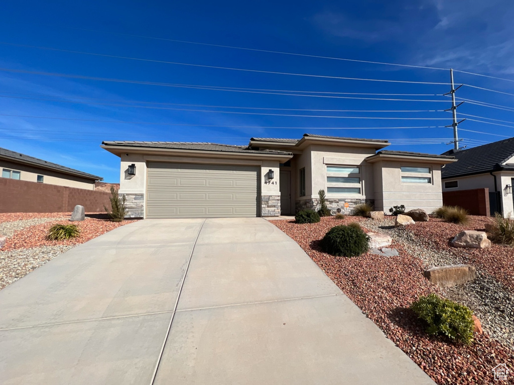 Prairie-style house with stone siding, a garage, stucco siding, fence, and driveway