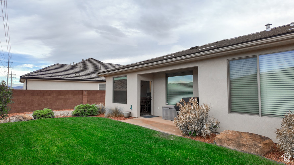 Rear view of house with stucco siding, fence, and a lawn