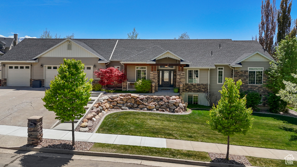 View of front of house with an attached garage, stone siding, driveway, a front yard, and a shingled roof