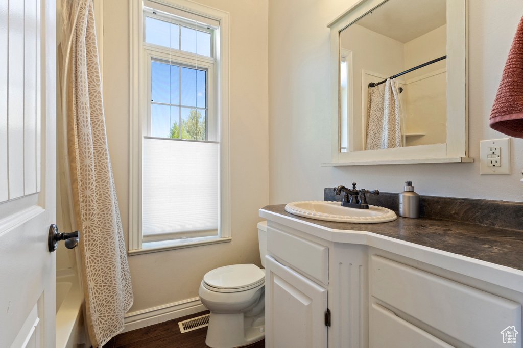 Full bathroom featuring toilet, wood finished floors, vanity, visible vents, and baseboards