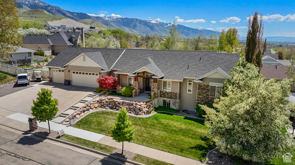 Ranch-style home featuring driveway, a front yard, a garage, stone siding, and roof with shingles