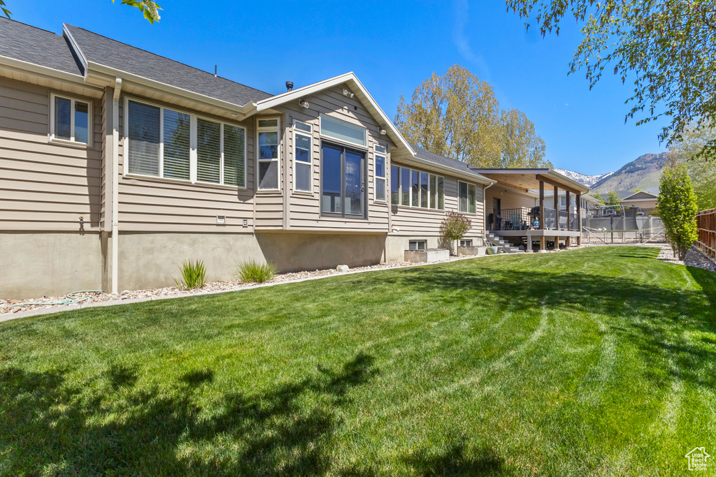 Back of house with fence, a mountain view, and a lawn