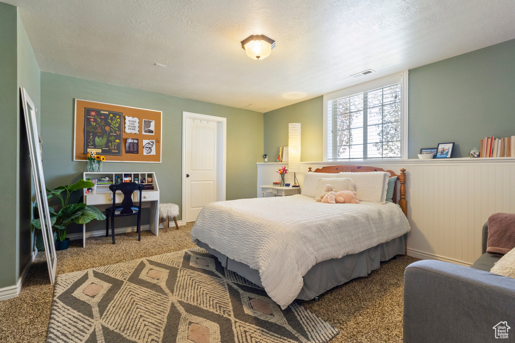 Bedroom with a textured ceiling, visible vents, wainscoting, and carpet floors