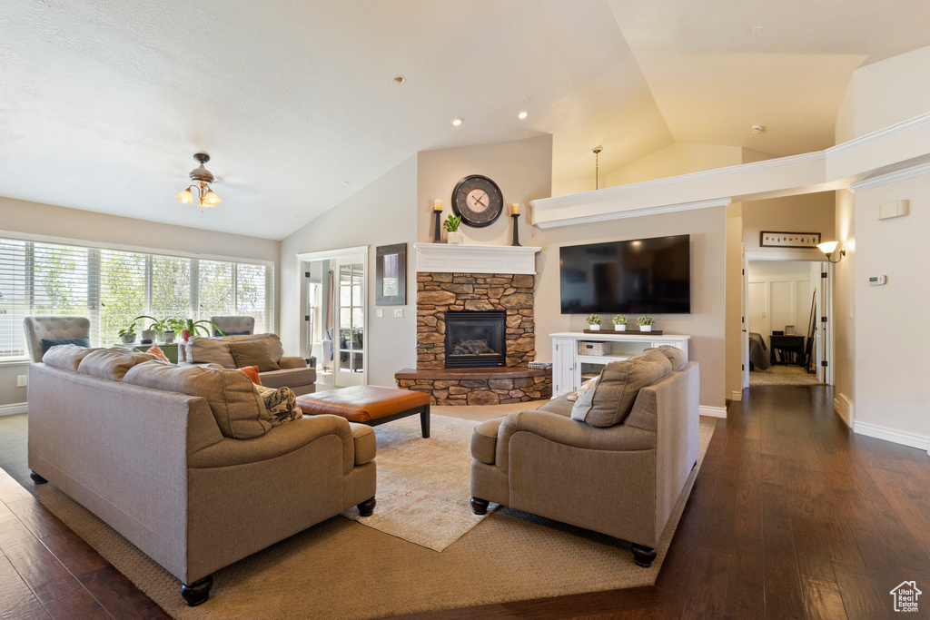 Living area featuring a ceiling fan, high vaulted ceiling, a fireplace, dark wood-type flooring, and baseboards