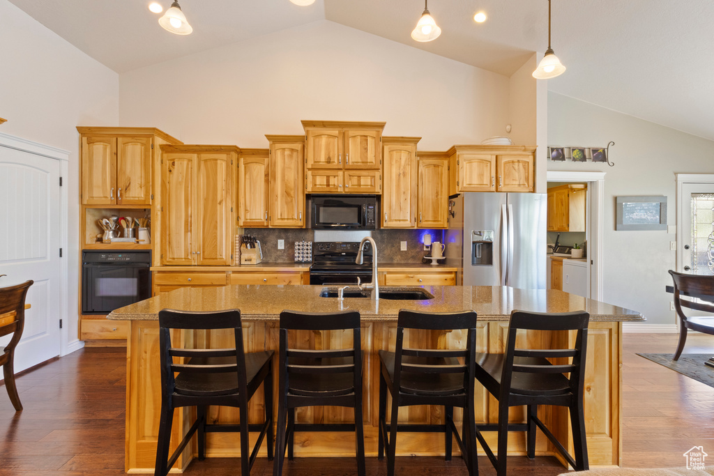 Kitchen featuring high vaulted ceiling, a sink, black appliances, and a center island with sink