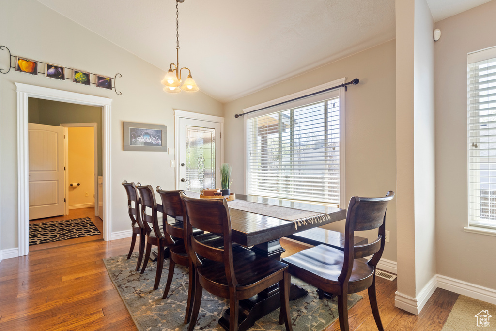 Dining area featuring lofted ceiling, a notable chandelier, a healthy amount of sunlight, and wood finished floors