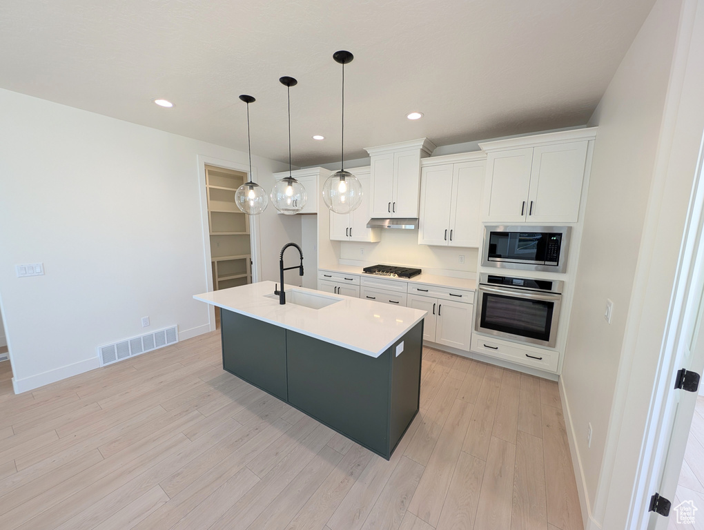 Kitchen featuring light wood-style flooring, visible vents, a sink, stainless steel appliances, and white cabinets