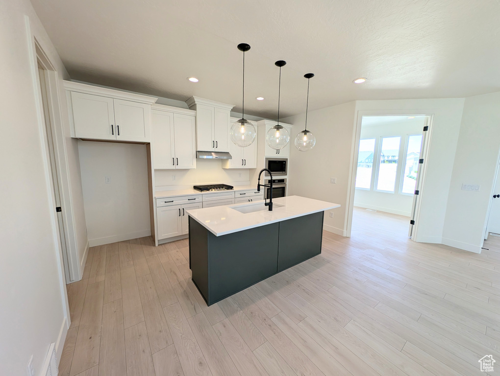Kitchen featuring under cabinet range hood, a sink, gas stovetop, white cabinets, and an island with sink