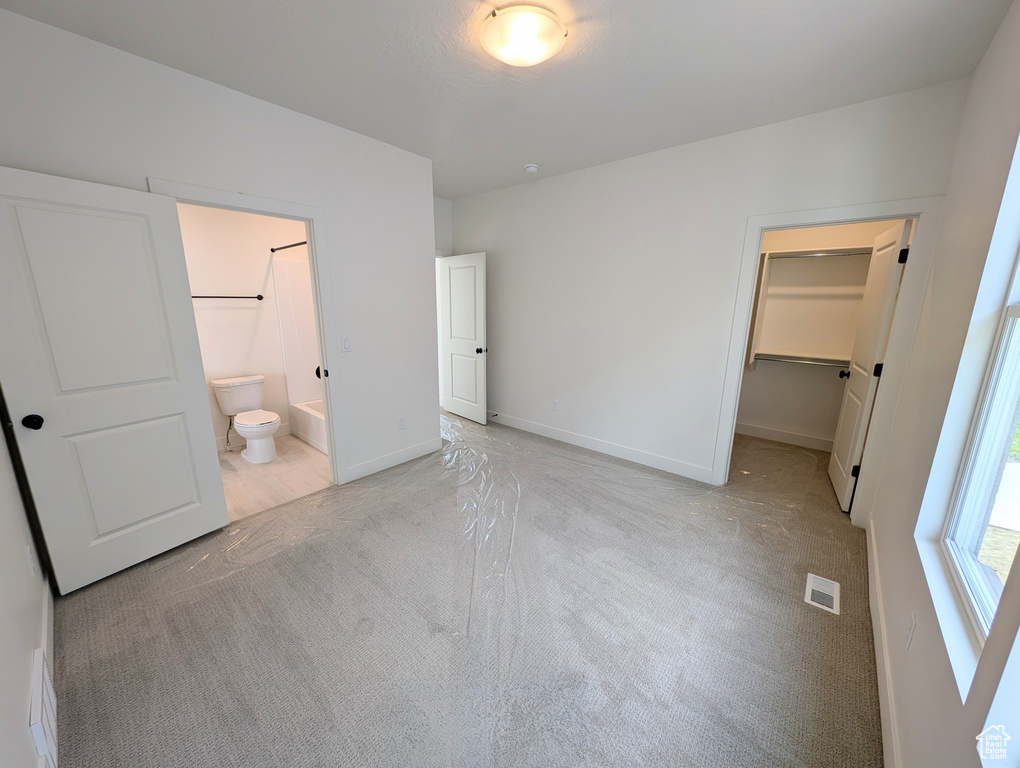 Unfurnished bedroom with a closet, visible vents, baseboards, light carpet, and a spacious closet