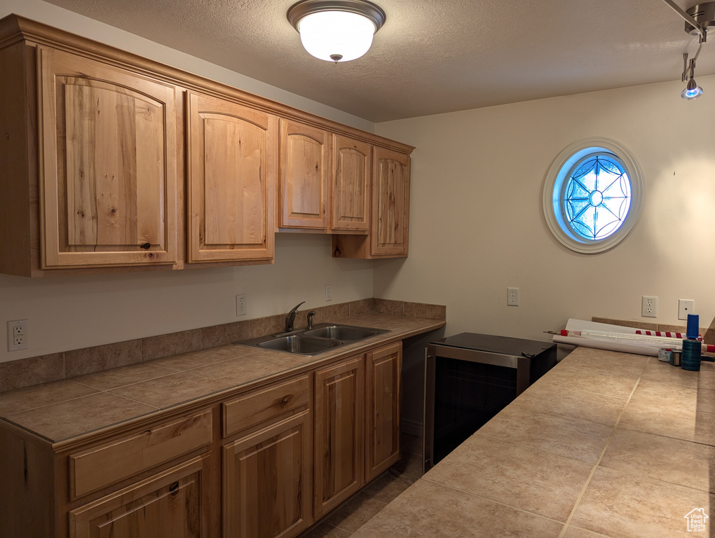 Kitchen featuring a textured ceiling, dark tile patterned flooring, tile countertops, and a sink