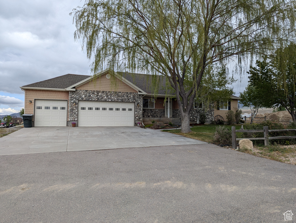 Ranch-style house with fence, an attached garage, stone siding, and driveway