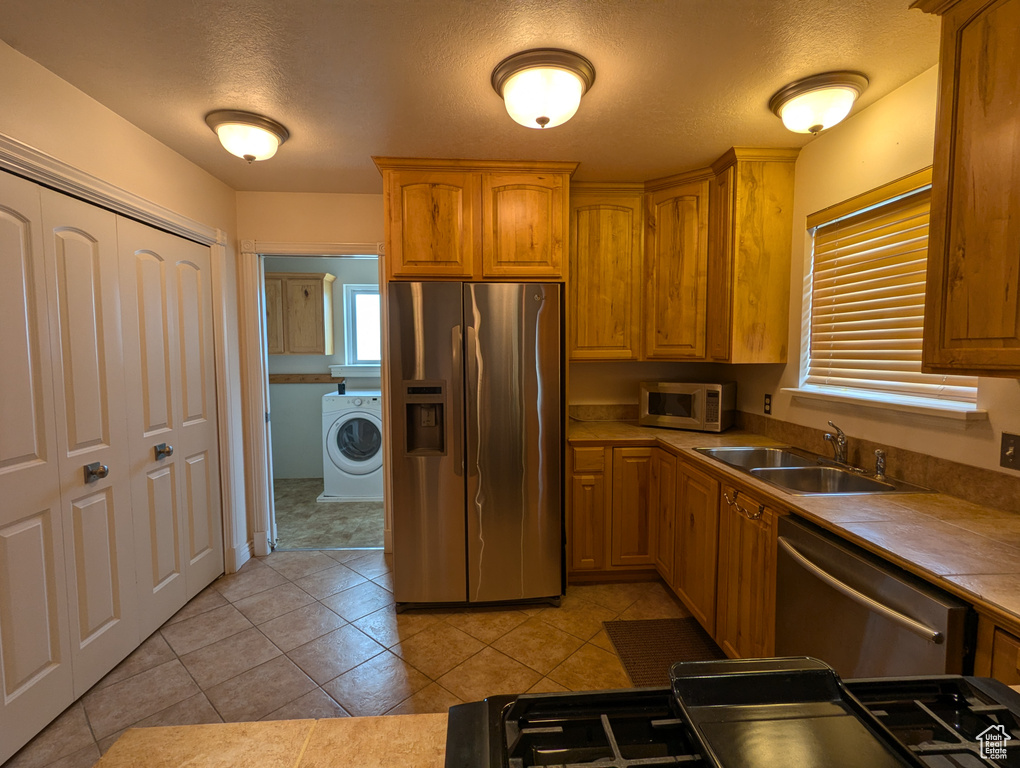 Kitchen with light tile patterned floors, a sink, stainless steel appliances, a healthy amount of sunlight, and washer / clothes dryer