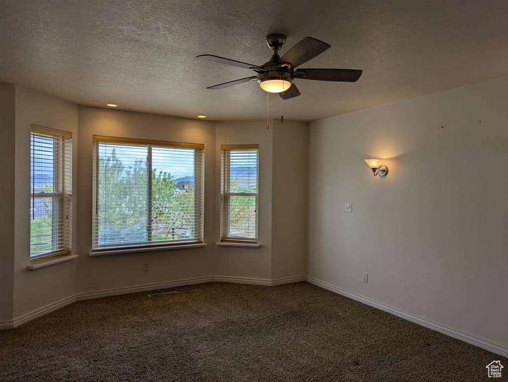 Carpeted spare room with ceiling fan, a textured ceiling, baseboards, and visible vents
