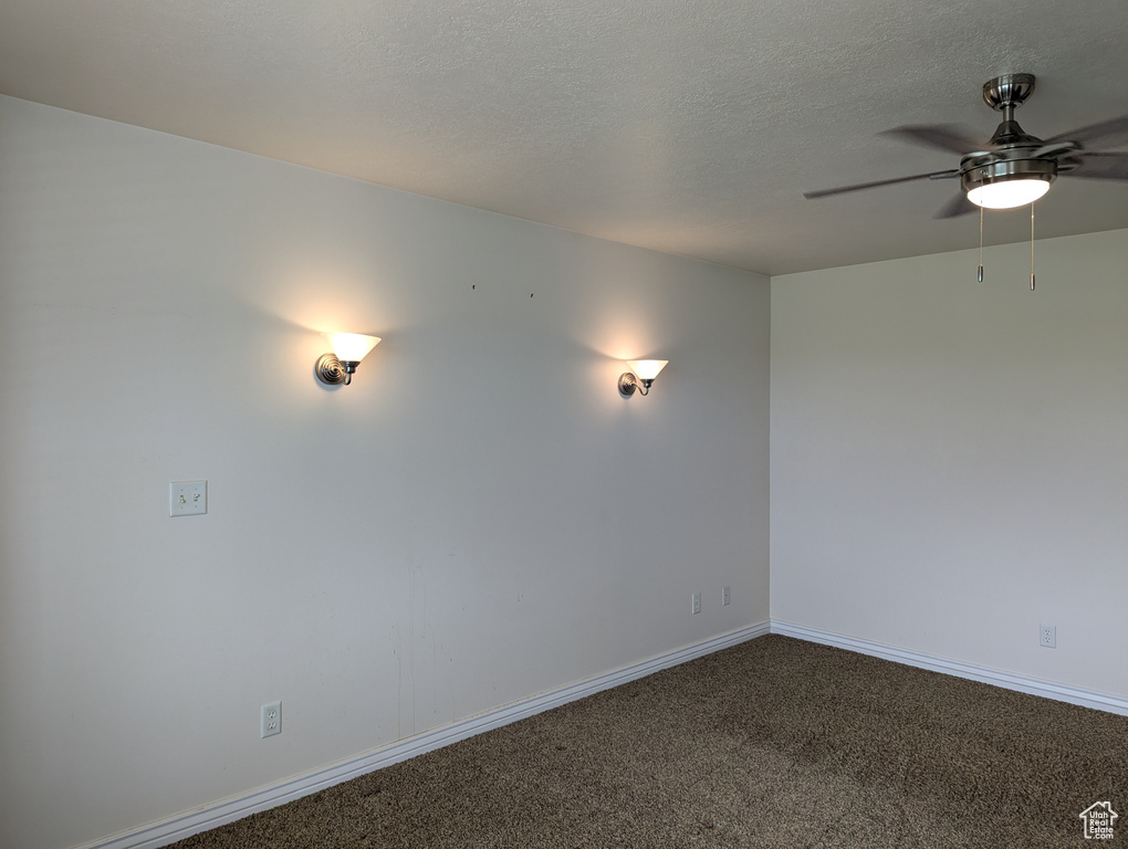 Empty room featuring a textured ceiling, dark colored carpet, baseboards, and ceiling fan