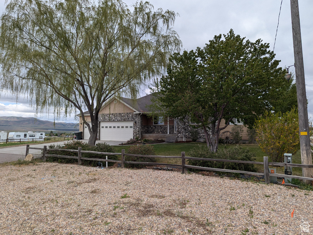 View of front of property with stone siding, a fenced front yard, a garage, and driveway