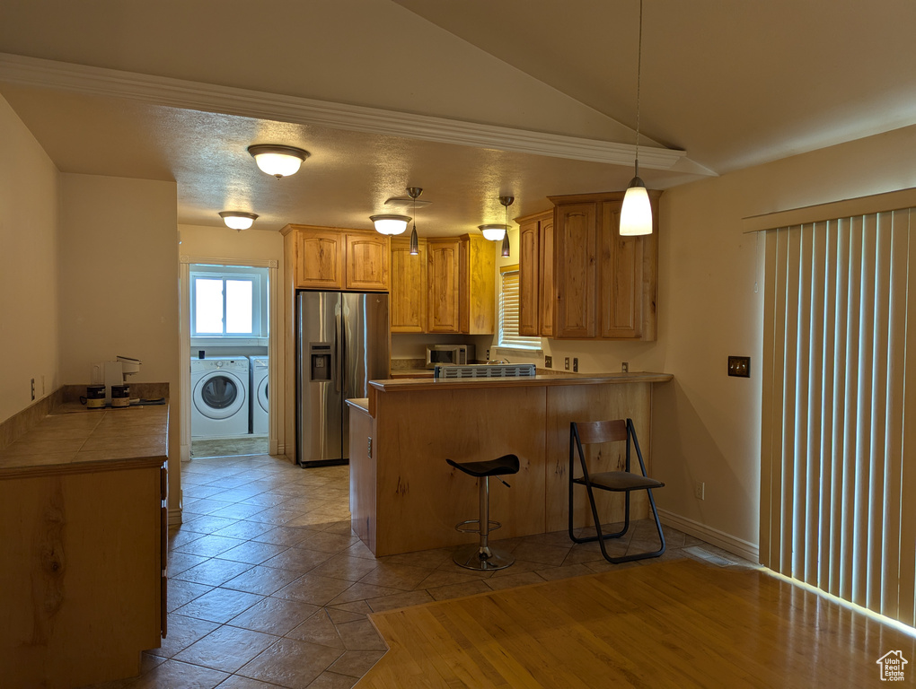 Kitchen featuring lofted ceiling, a breakfast bar, a peninsula, stainless steel appliances, and separate washer and dryer