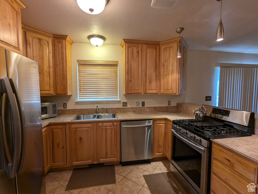 Kitchen with a sink, stainless steel appliances, visible vents, light tile patterned floors, and hanging light fixtures