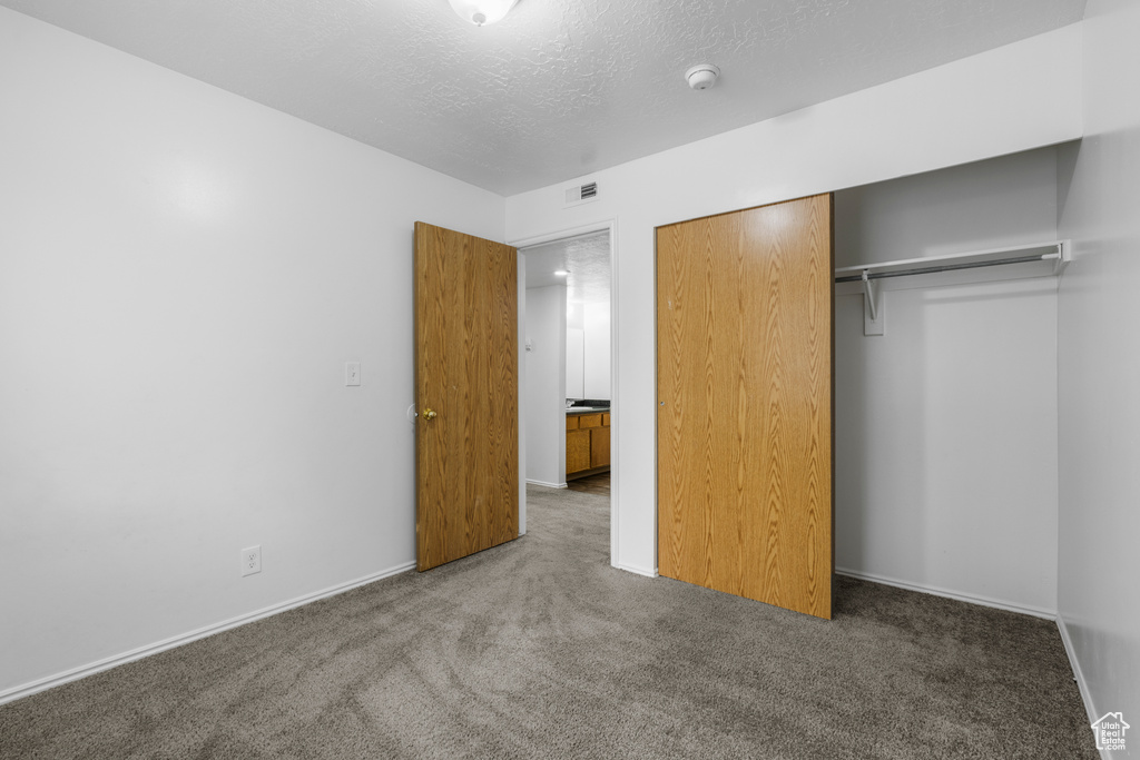 Unfurnished bedroom featuring a closet, a textured ceiling, baseboards, carpet flooring, and visible vents