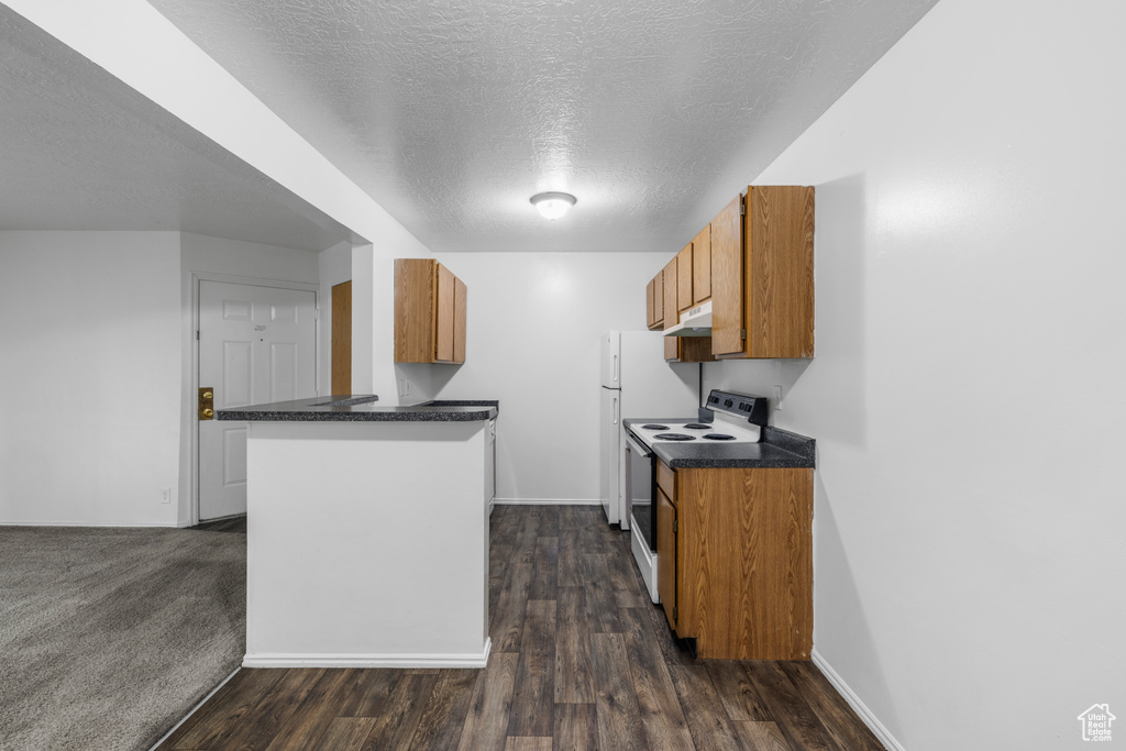 Kitchen with a textured ceiling, brown cabinetry, a peninsula, dark countertops, and electric range