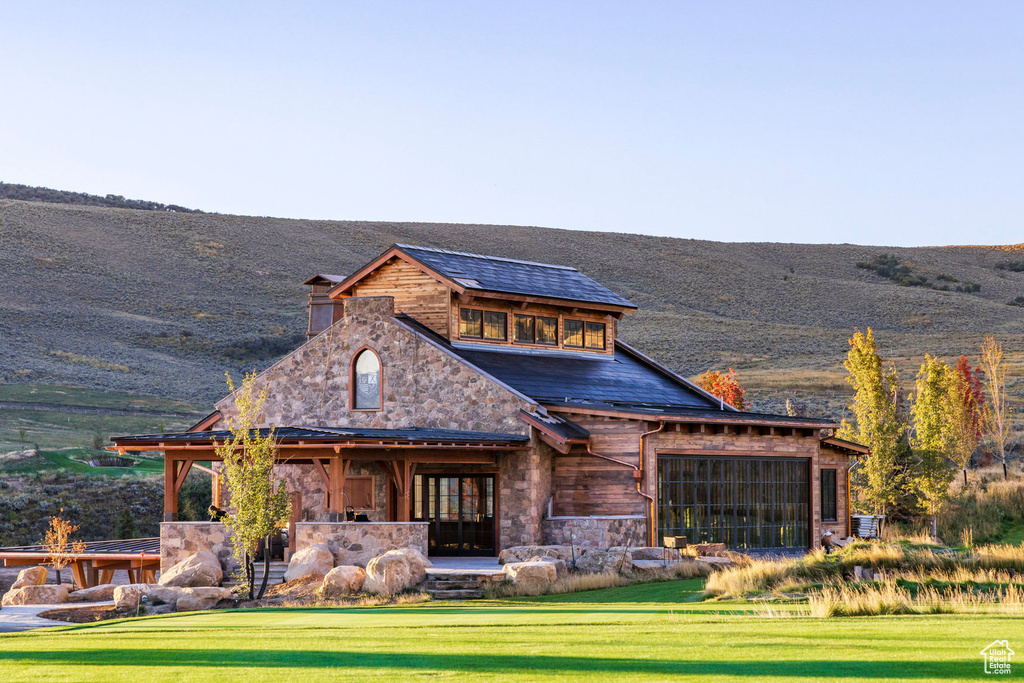 Back of property featuring stone siding, a mountain view, and a yard