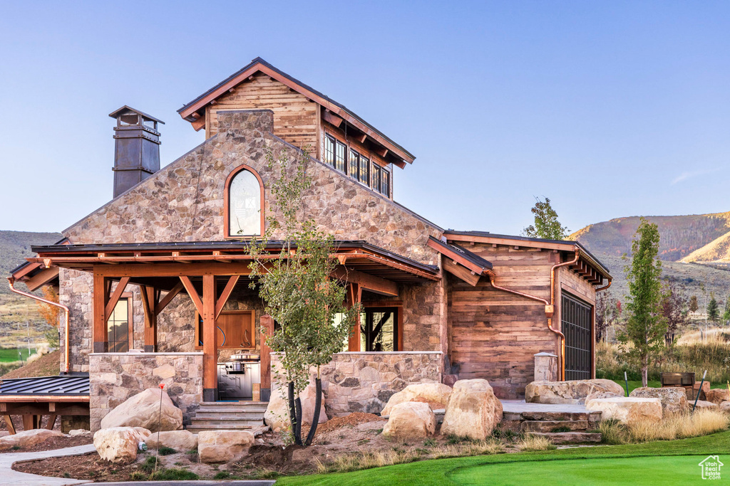 View of front of house with stone siding, a mountain view, and a chimney