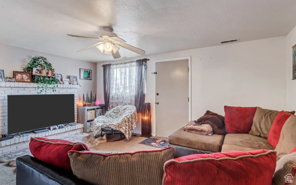 Carpeted living area with a fireplace, a ceiling fan, and visible vents