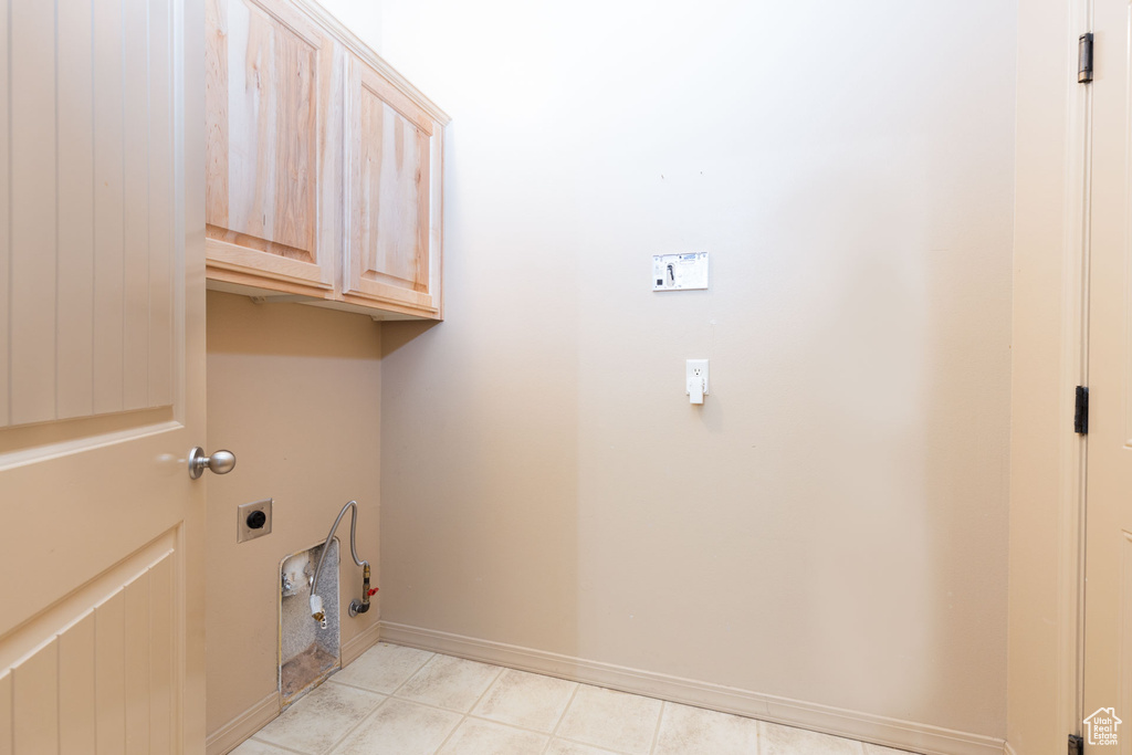 Clothes washing area featuring baseboards, hookup for an electric dryer, light tile patterned flooring, and cabinet space