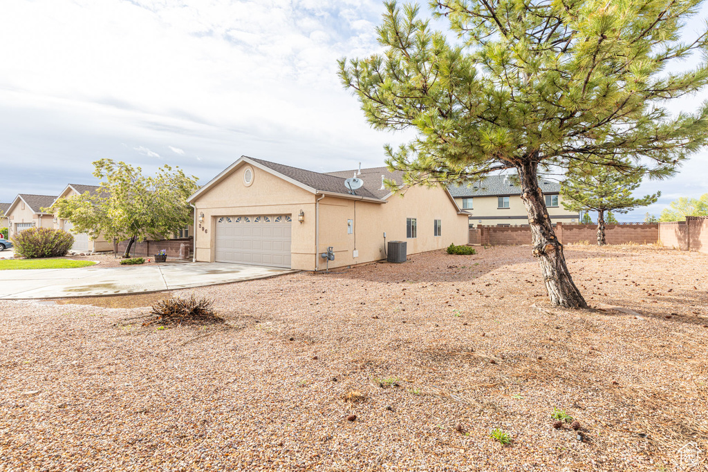 Exterior space with a garage, cooling unit, stucco siding, fence, and driveway