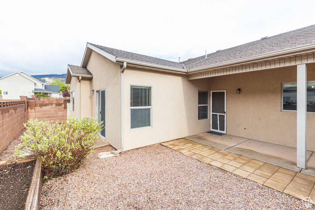Back of property with stucco siding, roof with shingles, fence, and a patio