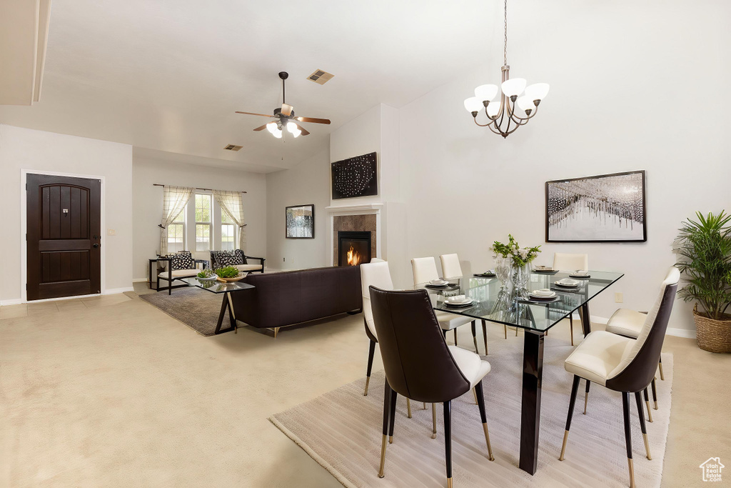 Dining area featuring lofted ceiling, ceiling fan with notable chandelier, visible vents, baseboards, and a tiled fireplace